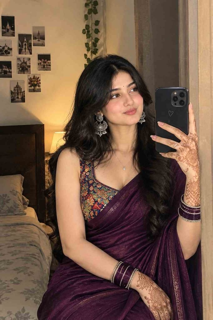 Woman wearing a deep wine-purple saree with colorful printed blouse, jewelry and mehndi